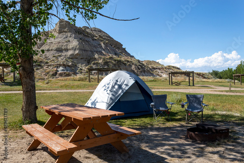 simple tent campsite with picnic table in Dinosaur provincial park southern alberta, grass and large rock formation in background with blue sky