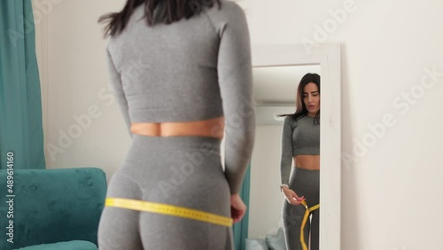 slim Woman waist Measuring With Tape at home. Beautiful woman checking success of weight loss program and measuring body in living room. slimming and weight loss concept.
