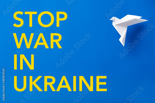 Stop war in Ukraine text in yellow on blue next to a white paper dove, peace photo