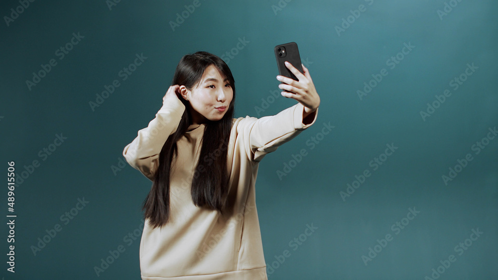 Pretty girl with long dark hair in beige hoodie makes selfie on her new phone Pretty girl with long dark hair in beige hoodie makes selfie on her new phone