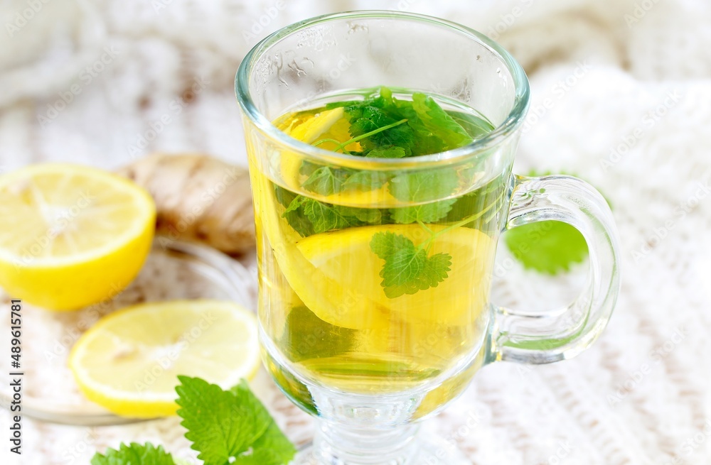 medicinal tea with lemon, lemon balm and ginger in a transparent glass on a light background, tea for colds and viruses