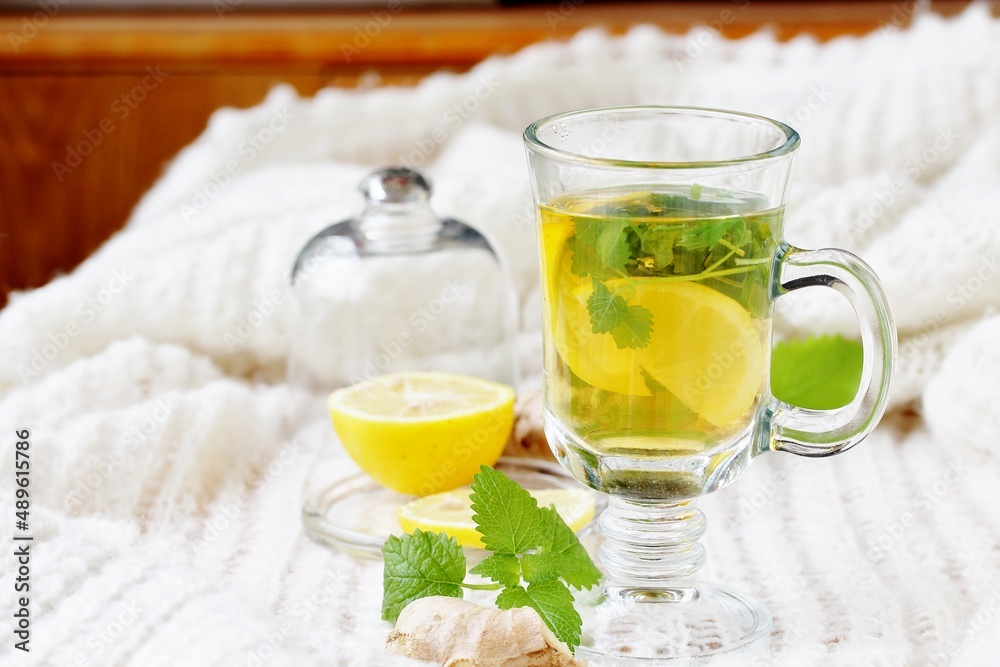 Fototapeta premium medicinal tea with lemon, lemon balm and ginger in a transparent glass on a light background, tea for colds and viruses