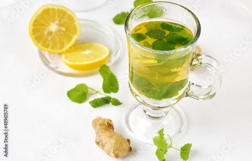 medicinal tea with lemon, lemon balm and ginger in a transparent glass on a light background, tea for colds and viruses