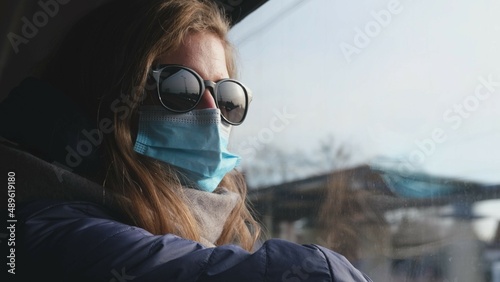 Blonde Caucasian Female Wearing Hygienic Face Mask Travelling on High Speed Passenger Train Looking at Landscapes Through Window of Railroad Car 