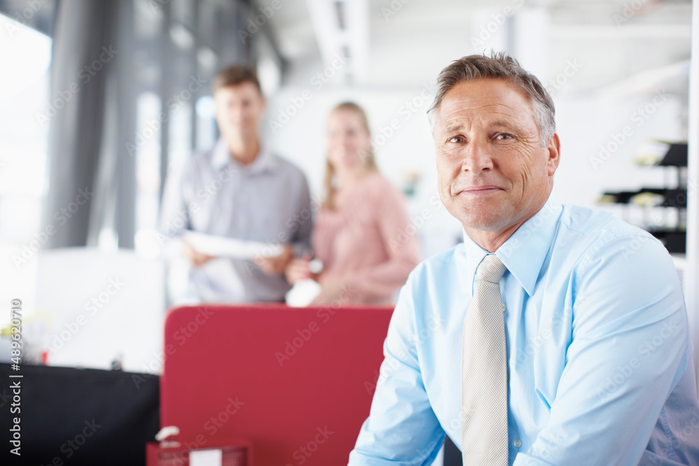 He relishes the challenges business throws at him. Portrait of a senior business manager smiling while his colleagues work in the background.