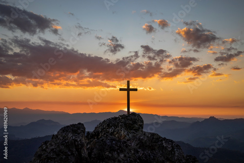 Christian cross on top rock mountain with bright sunbeam on the colorful sky background. Christian background concept