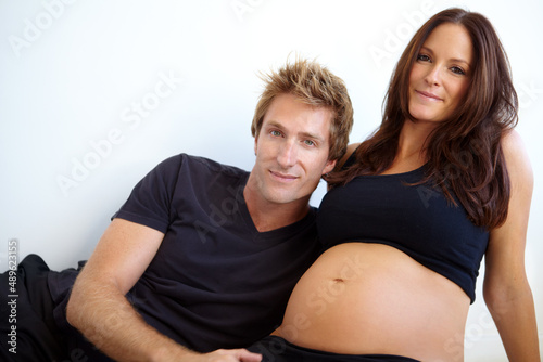 They cant wait to be parents. Young expecting couple sitting together against a white background.
