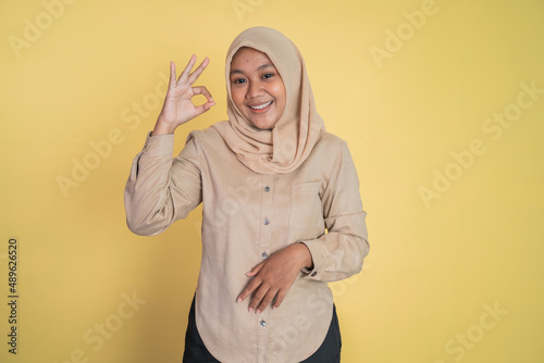 Young woman smiling with okay hand gesture on isolated background © Odua Images