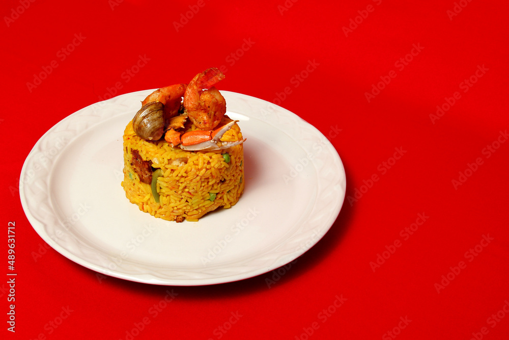 Arroz a la paella is a Spanish cuisine recipe made in a large pan with saffron, seafood such as shrimp, clam, sausage, chorizo on a white plate on a red background
Arroz a la paella is a Spanish cuisine recipe made in a large pan with saffron, seafood such as shrimp, clam, sausage, chorizo on a white plate on a red background