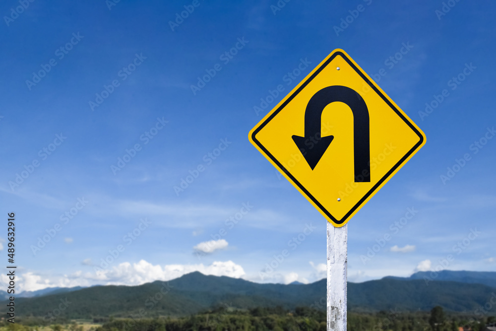 Traffic sign: left U-turn sign on cement pole beside the rural road with white cloudy bluesky background, copy space.