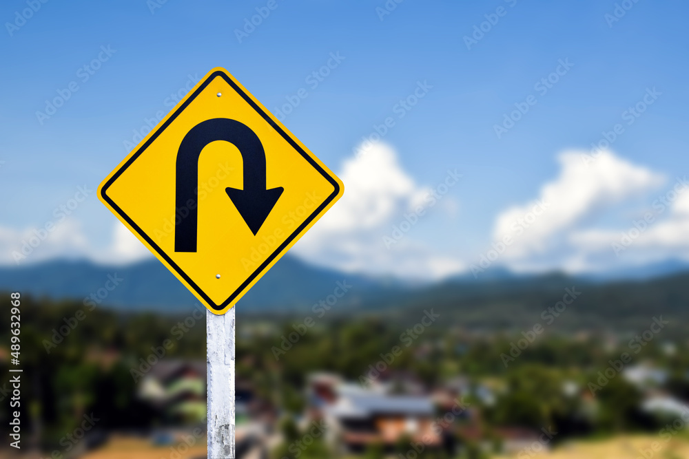Traffic sign: Right U-turn sign on cement pole beside the rural road with white cloudy bluesky background, copy space.