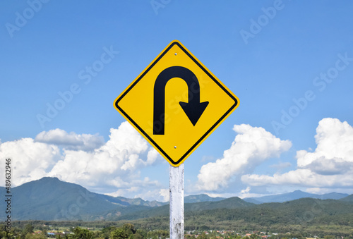 Traffic sign: Right U-turn sign on cement pole beside the rural road with white cloudy bluesky background, copy space.