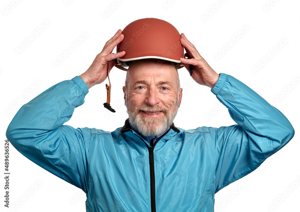 portrait of a happy senior male cyclist in late 60s wearing a new bright blue biking jacket and putting a helmet on, isolated on white