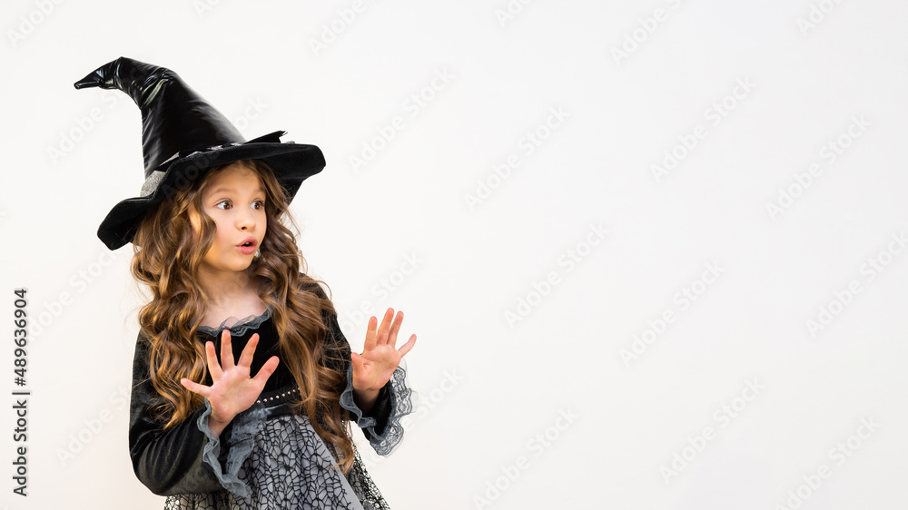 Surprised young witch on a white background. The costume of the sorceress for the carnival. A magician's hat on a little girl. A beautiful costume for magic. Surprised young witch on a white background. The costume of the sorceress for the carnival. A magician's hat on a little girl. A beautiful costume for magic.