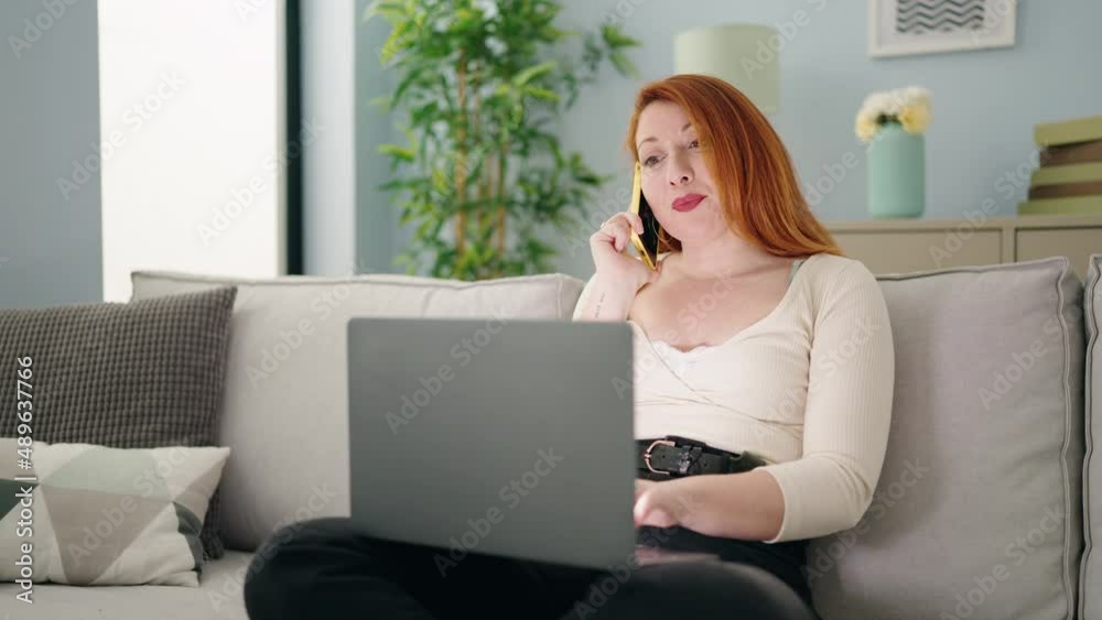 Young redhead woman using laptop and talking on the smartphone at home Young redhead woman using laptop and talking on the smartphone at home