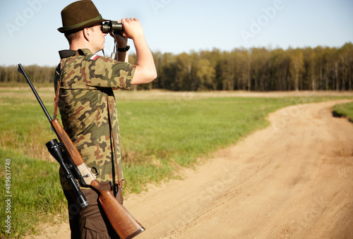 On the look out. A game ranger with his rifle looking through his binoculars in the outdoors with copyspace.