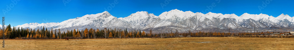 Panorama of nature. Mountainous terrain. Panoramic autumn landscape. A field in the foreground, a village forest and mountains in the distance. Mountain landscape.