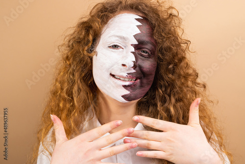 Pretty redhead curly woman fan footaball with painted face in Qatar flag keeping hand in front of her on yellow background. photo