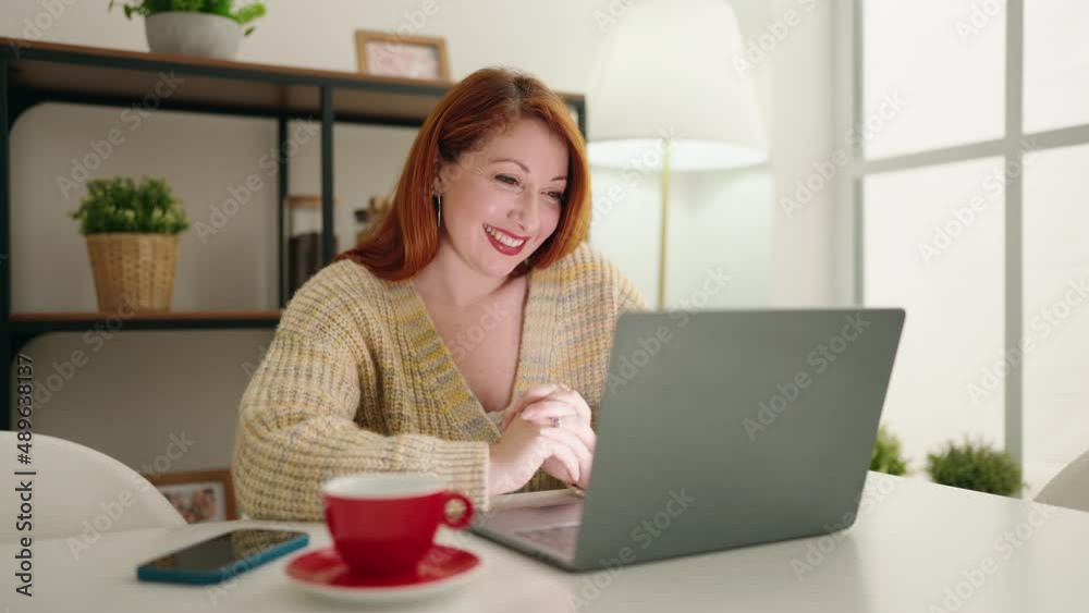 Young redhead woman having video call sitting on table at home Young redhead woman having video call sitting on table at home