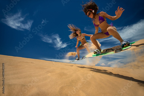 Kitesurf girls jumping on sandy beach with their arms raised against blue sky