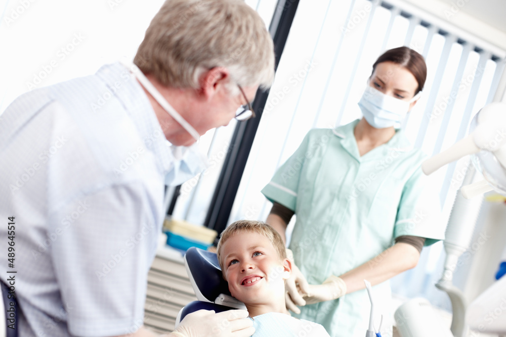 Dental treatment clinic. Portrait of young boy smiling at dentist with assistant in office. Dental treatment clinic. Portrait of young boy smiling at dentist with assistant in office.