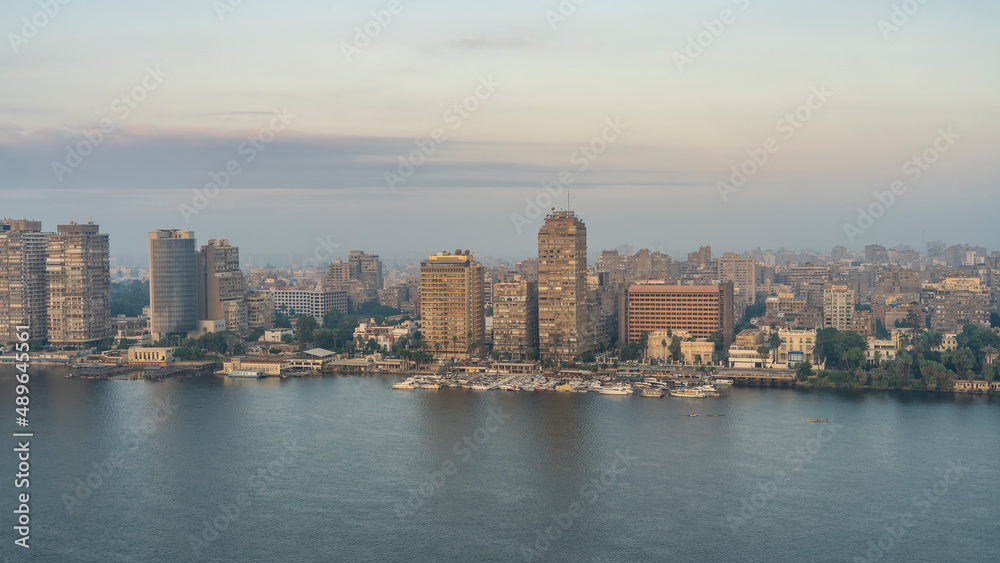 Morning in Cairo. The boats are parked on the bank of the Nile. City buildings, skyscrapers against the background of the dawn sky. Reflection on the calm surface of the water. Egypt