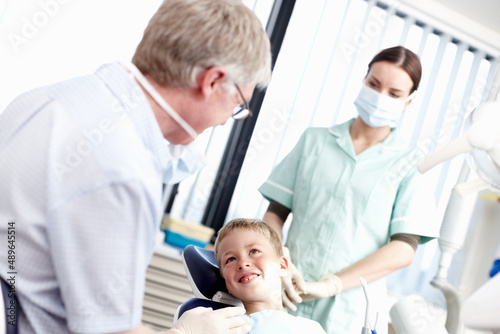 Dental treatment clinic. Portrait of young boy smiling at dentist with assistant in office.