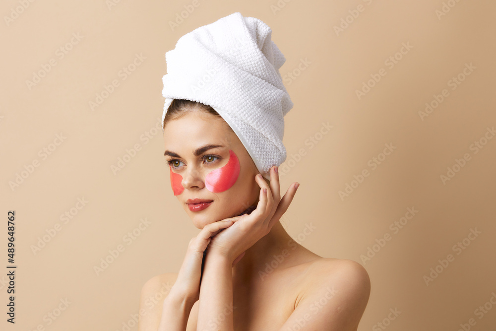 young woman pink patches on the face with a towel on the head beige background young woman pink patches on the face with a towel on the head beige background