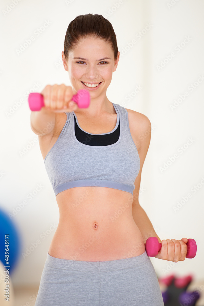 Shaping up. Portrait of a beautiful young woman training with a dumbbell in the gym. Shaping up. Portrait of a beautiful young woman training with a dumbbell in the gym.