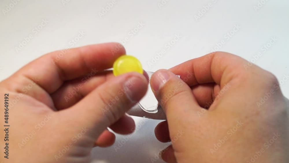 Close-up, hands unpacking a yellow pill from a package on a white background Close-up, hands unpacking a yellow pill from a package on a white background
