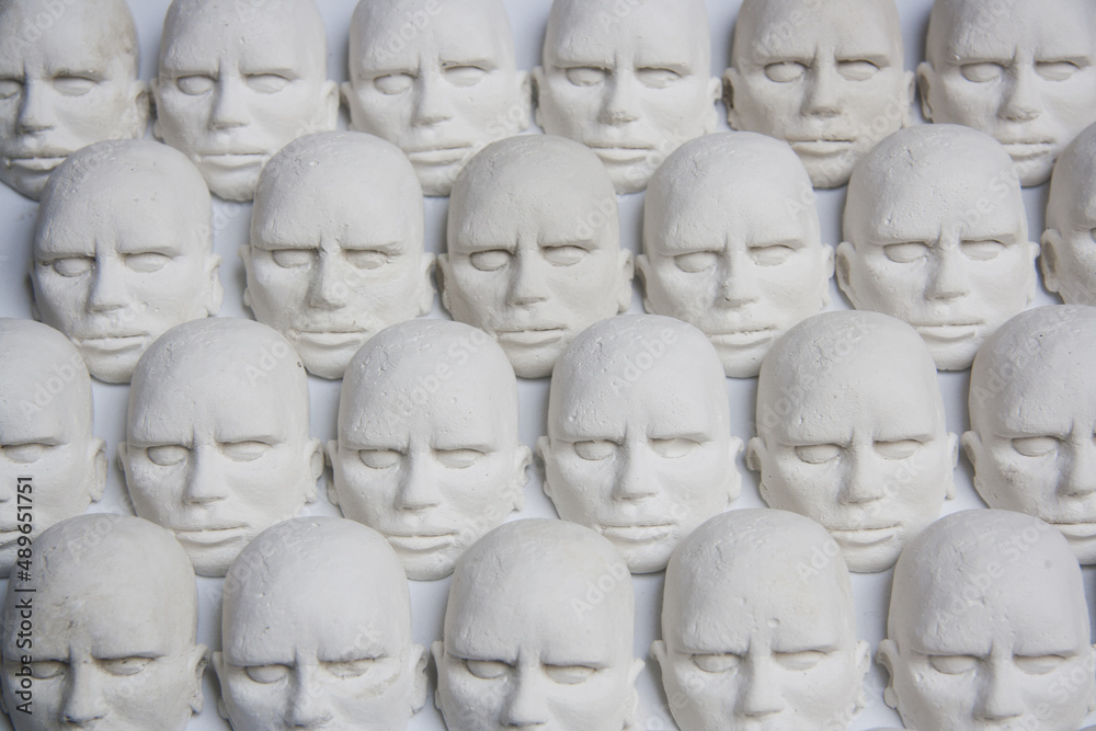 Small white sculptures of matching heads. Concept of mass, unique thinking and conformism.