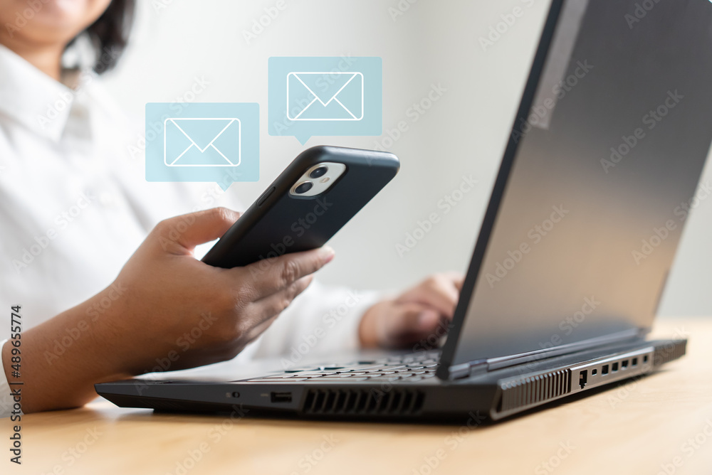 Woman hand holding mobile phone receive or send email icon on working desk with laptop Woman hand holding mobile phone receive or send email icon on working desk with laptop