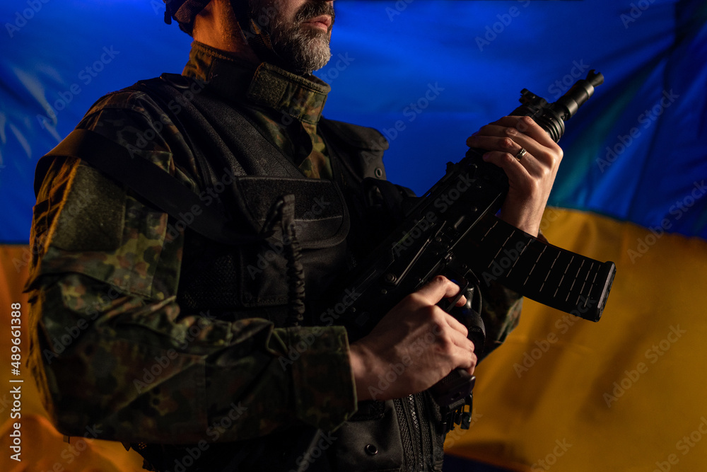 Close-up of soldier in military uniform holding weapon with Ukraine flag in background. Close-up of soldier in military uniform holding weapon with Ukraine flag in background.