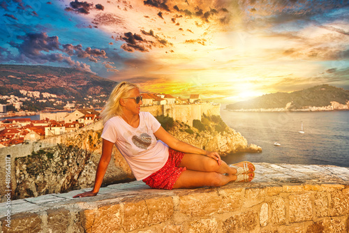 Woman sitting at sunset on Fort Lovrijenac fortress. On the West Harbour of Dubrovnik in Croatia. View of Dubrovnik historic city walls with Fort Bokar. Croatian vacation in Dalmatia and UNESCO Site. photo