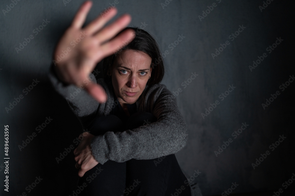 Depressed mid-adult woman, alone in darkness, looking at camera, stop the war concept.