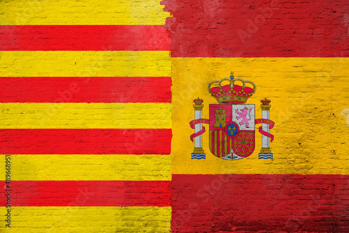 Full frame photo of a weathered flags of Catalonia and Spain painted on a plastered brick wall.
