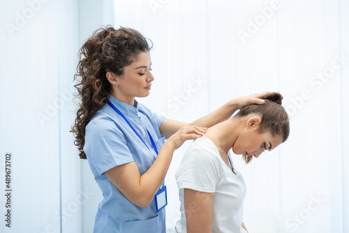 Licensed chiropractor or manual therapist doing neck stretch massage to relaxed female patient in clinic office. Young woman with whiplash or rheumatological problem getting professional doctor's help photo