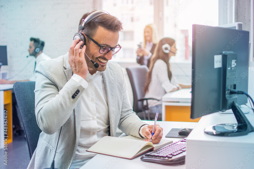 Handsome male call center operator in headset working in modern office. Hotline support service concept