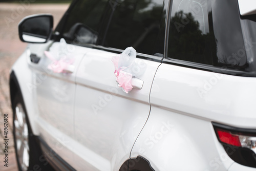 Wedding decor on the car handle. Flower decoration with ribbons on a white car © Artem Zakharov