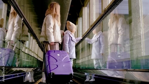 Mom and daughter go up the escalator to the building of the station