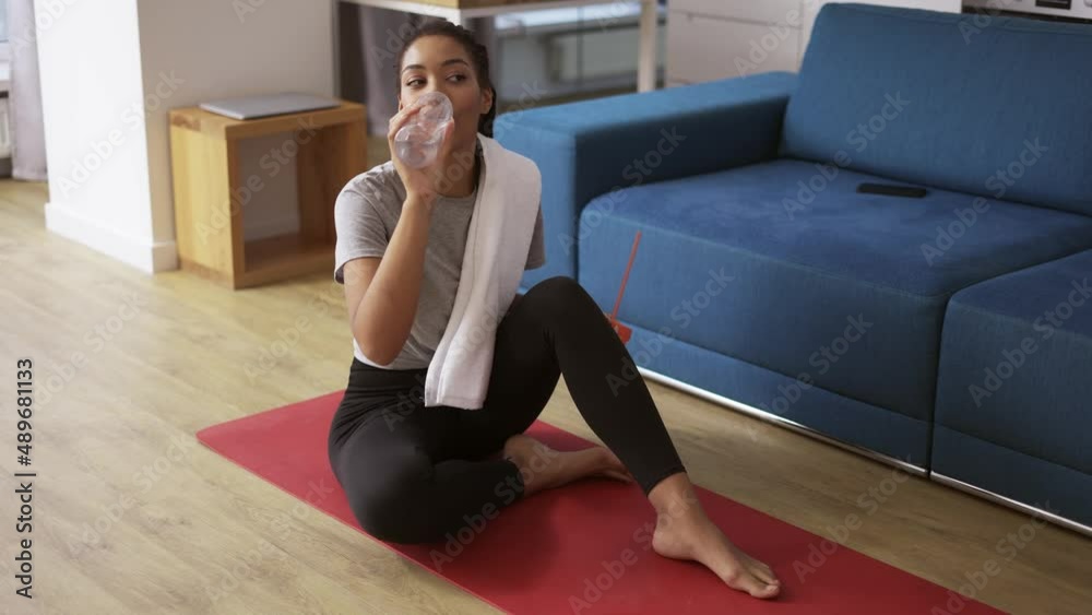 Sporty african american woman drinking water after workout at home on yoga mat Sporty african american woman drinking water after workout at home on yoga mat