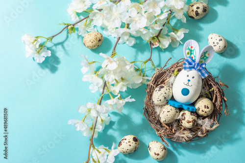 Happy Easter blue background with blooming cherry, quail eggs in a nest and cute rabbit