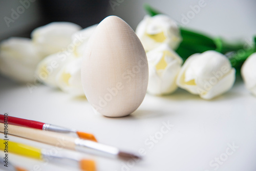 A close-up of a white Easter egg against a tulip background, tassels lying nearby. Holiday concept
