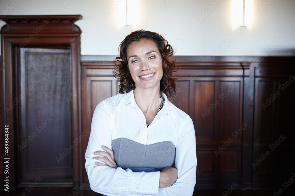 Ready for the judge. Attractive female legal person standing with her arms folded and smiling widely in the courtroom. Ready for the judge. Attractive female legal person standing with her arms folded and smiling widely in the courtroom.