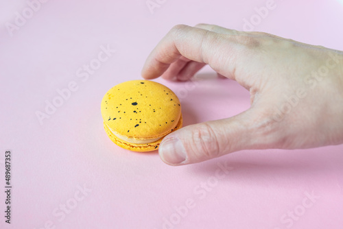 Hand takes yellow macaroon, dessert on pink background