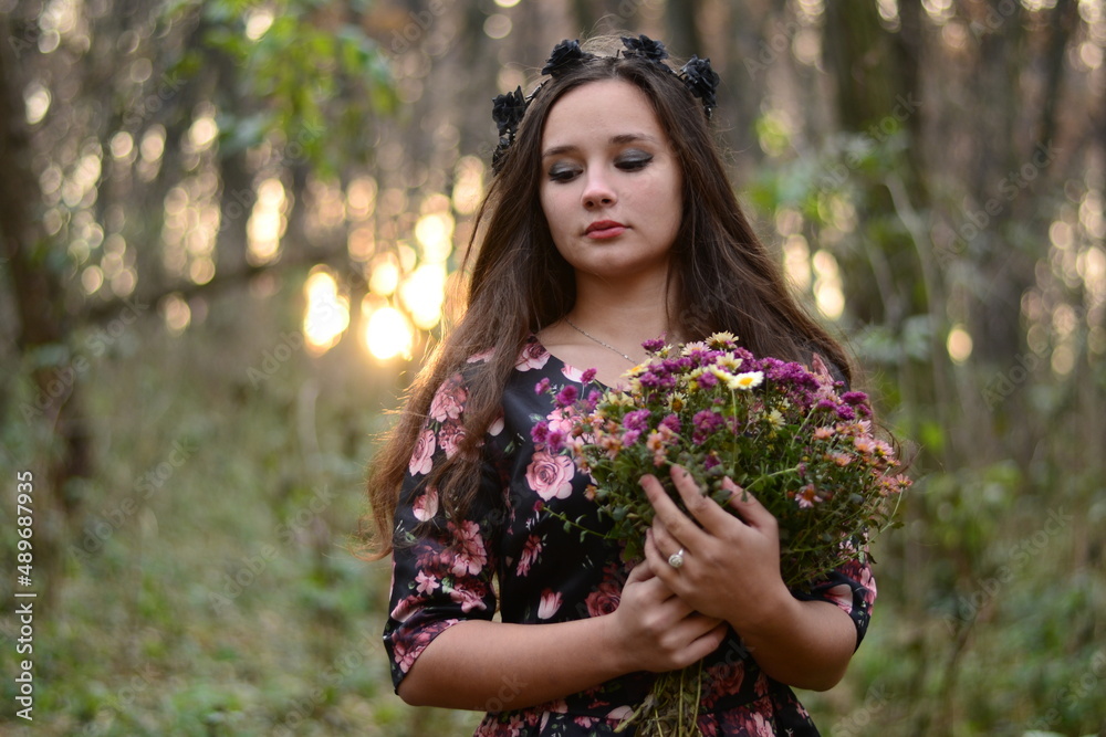 brown haired girl in a black dress in a floral print with a black wreath with roses and thorns on her head in the forest in the evening in autumn brown haired girl in a black dress in a floral print with a black wreath with roses and thorns on her head in the forest in the evening in autumn