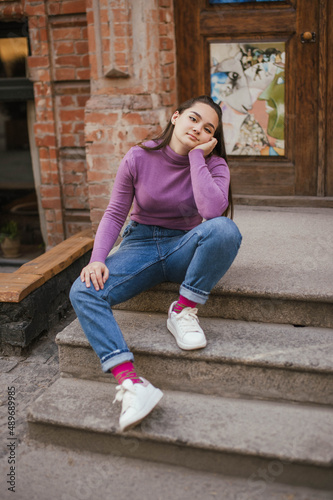 Photo of a brown-haired girl in a lilac Golf and jeans on the street in the city © Alina Belych