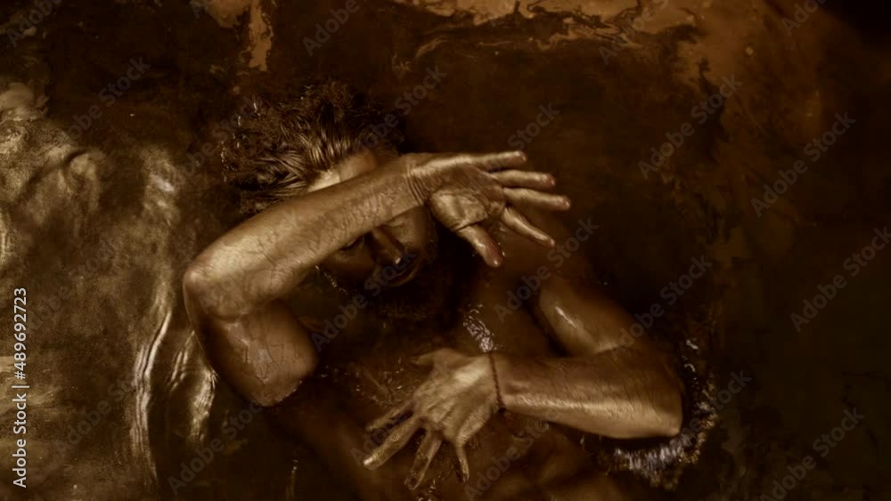 sexy man is swimming and dancing in golden water, naked muscular torso and arms