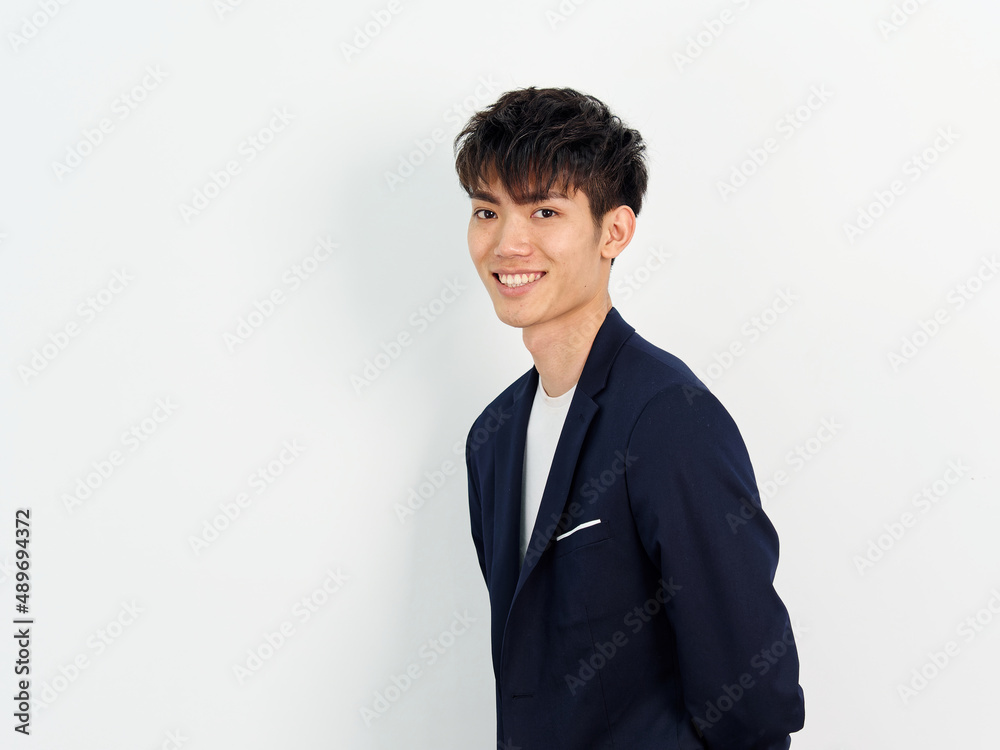 Portrait of handsome Chinese young man in dark blue leisure suit posing against white wall background. Arms on back and looking at camera, looks confident, side view. Portrait of handsome Chinese young man in dark blue leisure suit posing against white wall background. Arms on back and looking at camera, looks confident, side view.