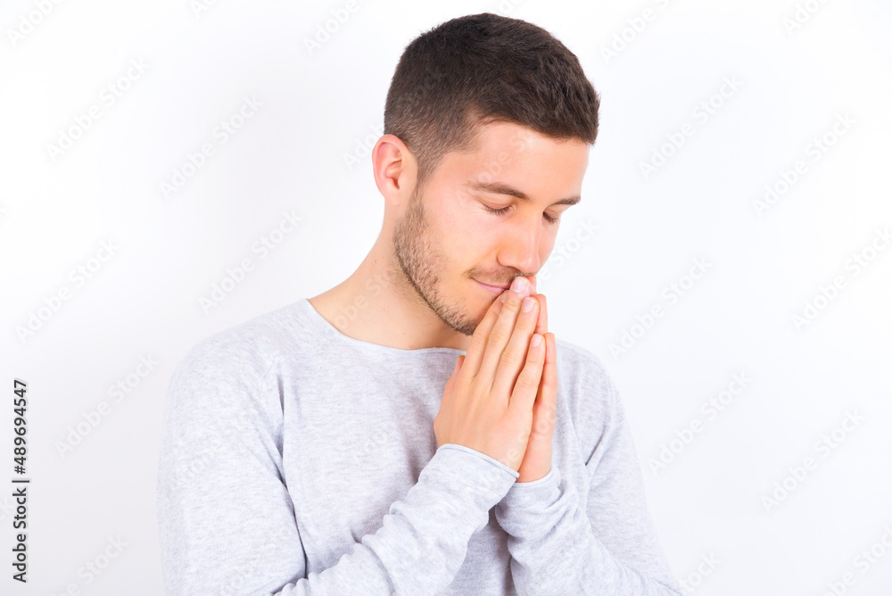 Overjoyed young caucasian man wearing grey sweater over white background laughs joyfully and keeps palms pressed together hears something funny Overjoyed young caucasian man wearing grey sweater over white background laughs joyfully and keeps palms pressed together hears something funny